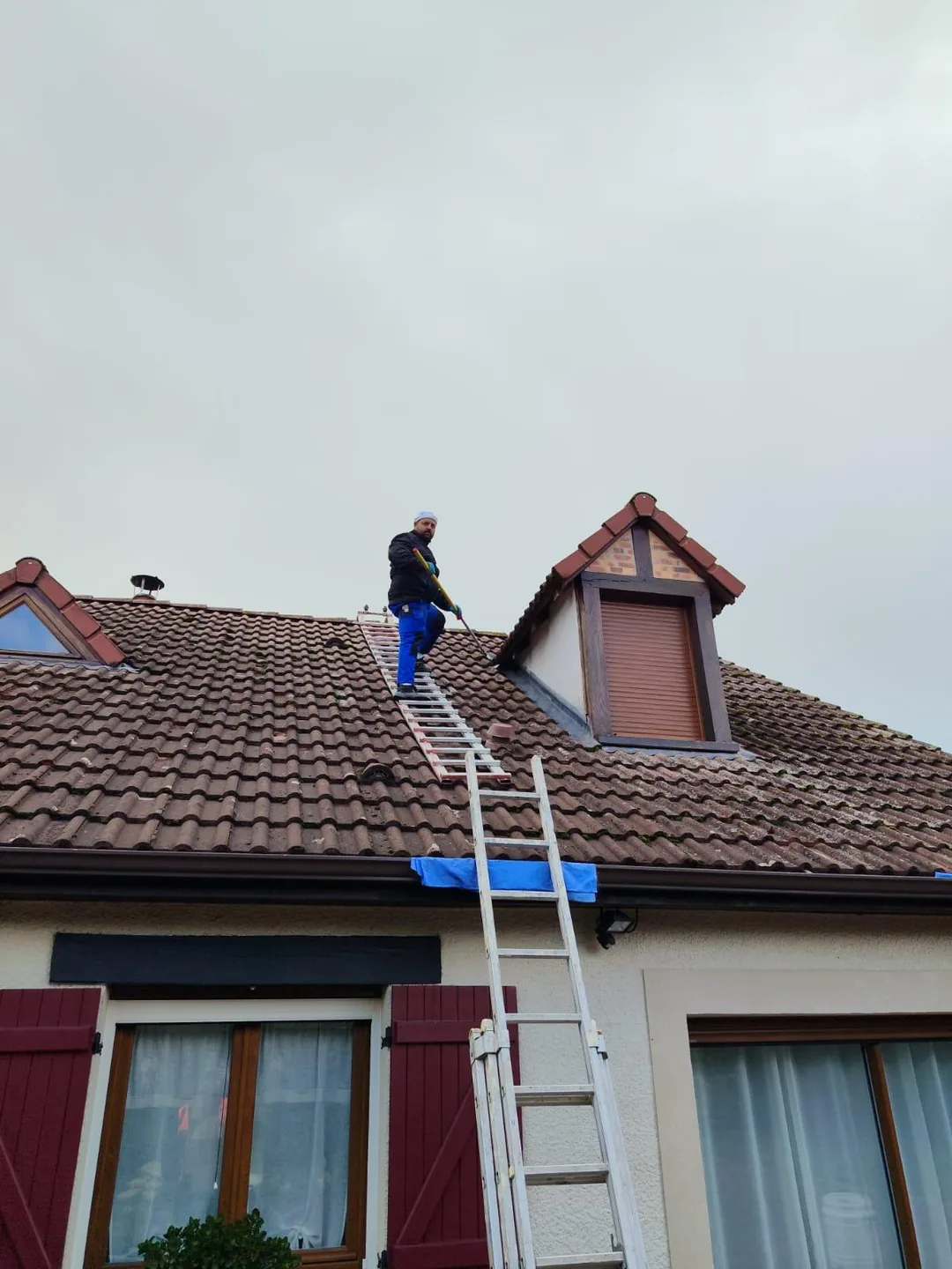 Professionnel au travail sur une toiture, depuis une échelle.
